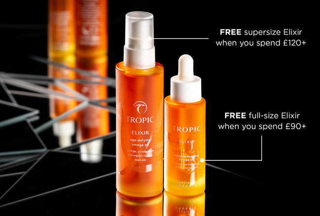 Two bottles of Tropic Elixir face oils on a mirrored surface with text highlighting a free full-size or supersize Elixir offer when you spend £90 or £120.